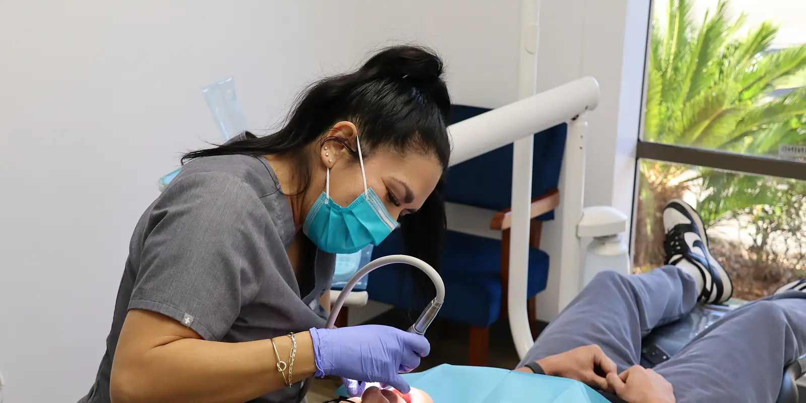 A hygienist cleaning a patient’s teeth in a bright treatment room; the patient shown is a model